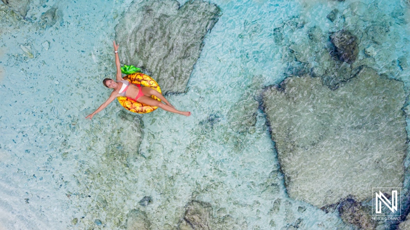 A woman relaxes on a colorful float in crystal clear water, surrounded by rocky formations during a sunny day at a tropical beach