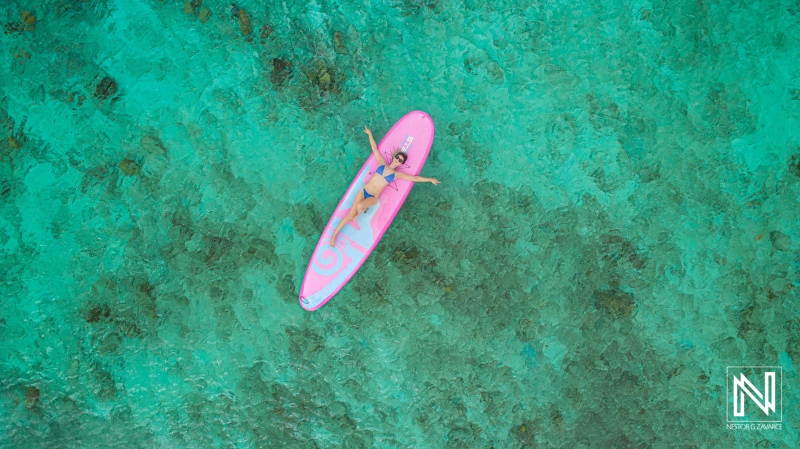 A woman enjoys paddle boarding on a vibrant turquoise sea near a coral reef during a sunny day at the beach