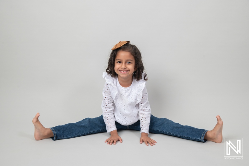 A cheerful girl performing a split in a studio setting with neutral backdrop, showcasing joy during a playful moment