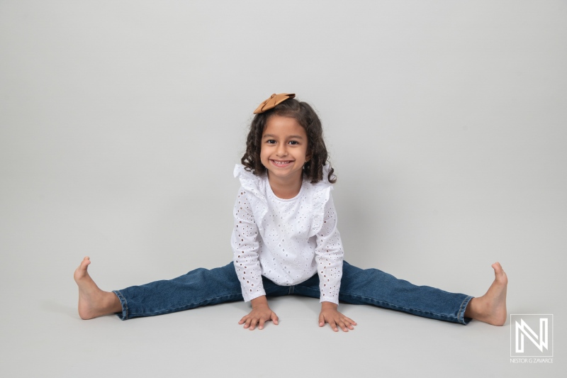 A cheerful girl performing a split in a studio setting with neutral backdrop, showcasing joy during a playful moment