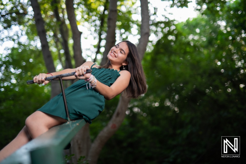 A girl enjoying a sunny day at the park swinging on a playground bar surrounded by greenery and trees in the background, creating a lively and cheerful atmosphere