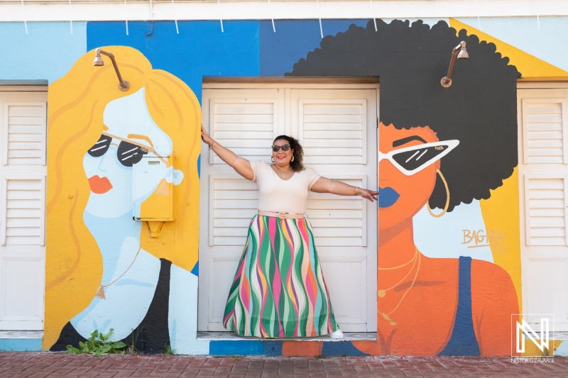 Bright mural backdrop featuring two stylish women with sunglasses beside a joyful woman in a colorful skirt posing in a vibrant street setting