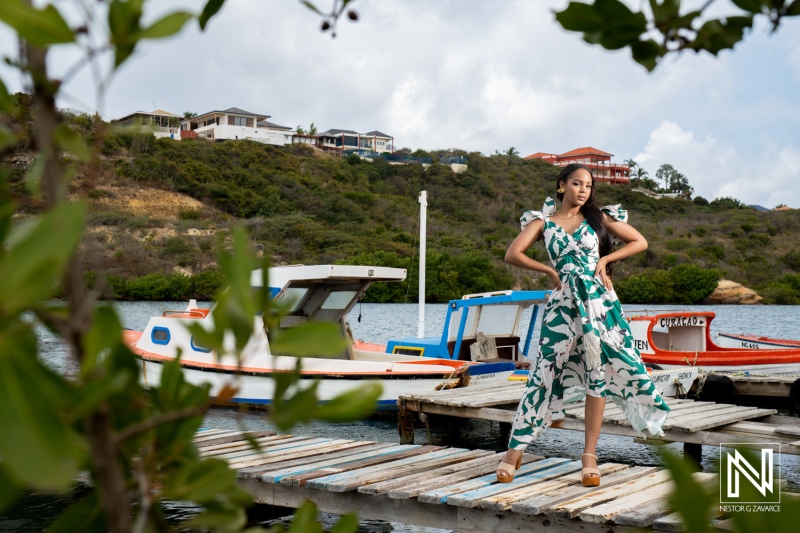 A woman poses gracefully by colorful boats on a wooden dock surrounded by lush greenery on a sunny day in a tropical coastal location