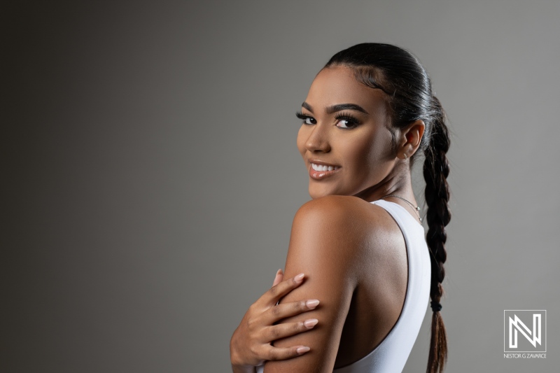 Young woman with long braided hair poses confidently in a modern studio setting while smiling warmly, showcasing her beauty and style