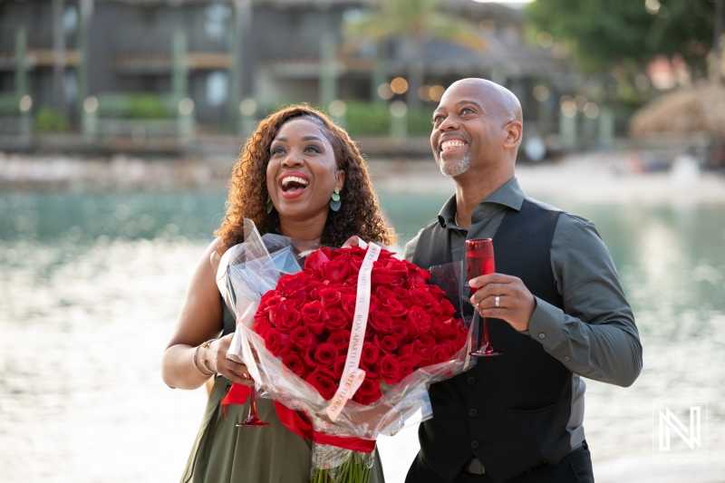 Couple celebrates wedding proposal with roses and champagne at Avila Beach Hotel in Curacao during sunset by the water