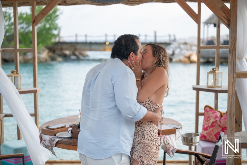 Couple shares kiss during wedding proposal at Baoase Luxury Resort in Curacao near the water while surrounded by romantic setup