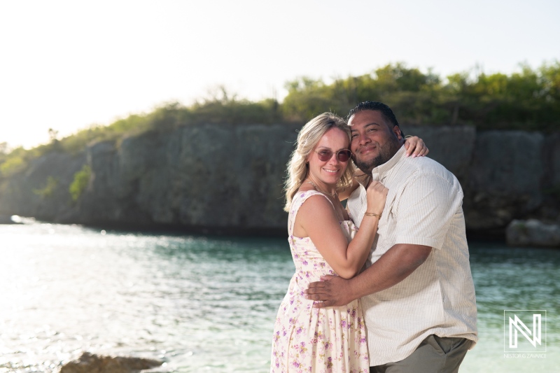 A joyful couple enjoying a romantic moment by the beach during sunset while embracing each other with a backdrop of rocky cliffs and serene water