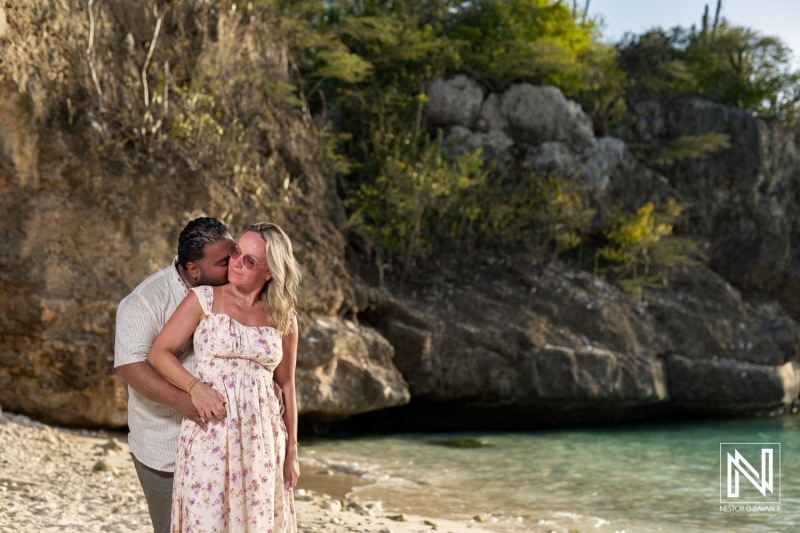 Couple embracing on a tropical beach by the shoreline during a sunny afternoon, with cliffs in the background and lush greenery surrounding them