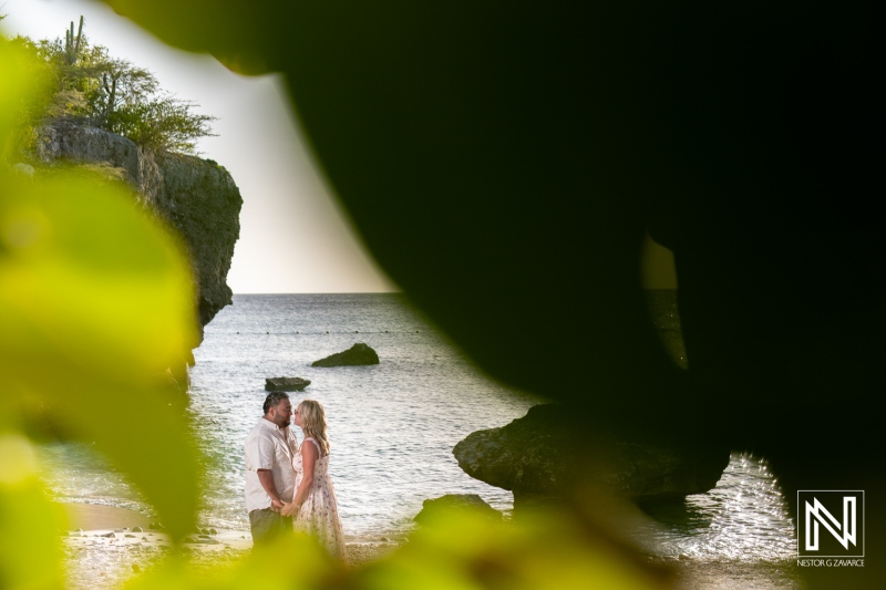 A couple embraces on a serene beach at sunset surrounded by natural rock formations in a tropical paradise