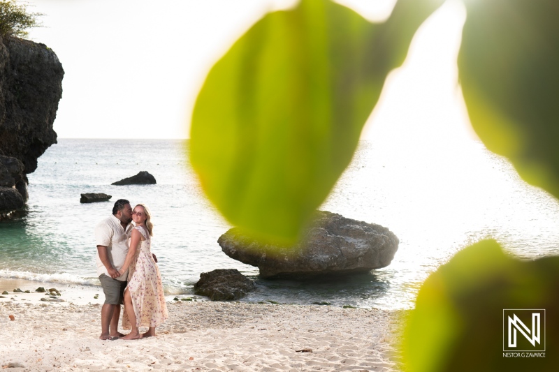 Young couple enjoying a romantic moment on a tropical beach at sunset, surrounded by lush greenery and serene waves lapping at the shore