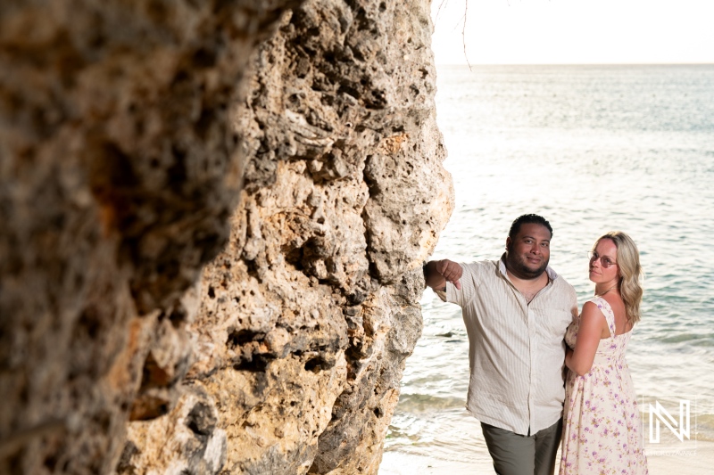 A romantic couple poses by a rocky shoreline at sunset, showcasing their love while enjoying a tranquil beach setting in a coastal paradise