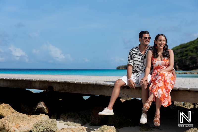 A Couple Enjoying a Sunny Day on a Wooden Pier by the Beach, Surrounded by Clear Blue Waters and Lush Greenery in a Tropical Paradise