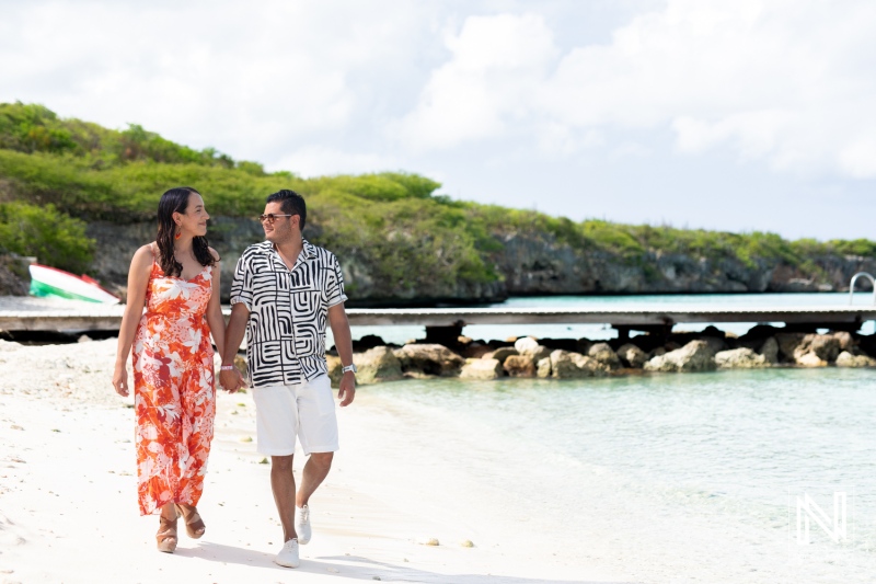 A Couple Strolls Hand in Hand Along a Picturesque Beach, Enjoying a Sunny Day by the Clear Water and Lush Greenery in the Background