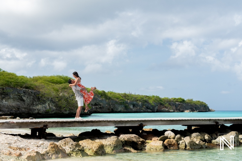 A Couple Joyfully Dances on a Wooden Dock by the Turquoise Waters of a Tropical Beach Surrounded by Lush Greenery on a Sunny Day