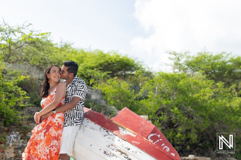 Couple Enjoying a Romantic Moment by an Abandoned Boat on a Sunny Day, Surrounded by Lush Greenery in a Coastal Area