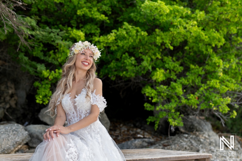 A Bride in a Flowing Lace Gown Sits on a Wooden Bench Surrounded by Lush Greenery, Enjoying a Serene Moment in Nature During Her Wedding Day