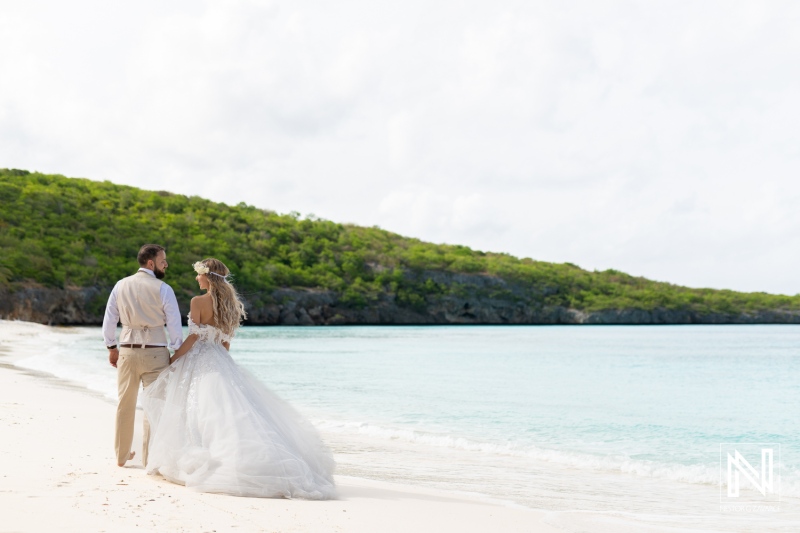 A Couple Stands Hand in Hand on a Serene Beach in a Tropical Location, Illuminated by Soft Sunlight, as the Ocean Waves Gently Lap Against the Shore During Their Wedding Celebration