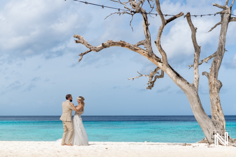 A Beautiful Beach Wedding Ceremony Takes Place Beneath a Weathered Tree With Stunning Turquoise Waters in the Background on a Sunny Day