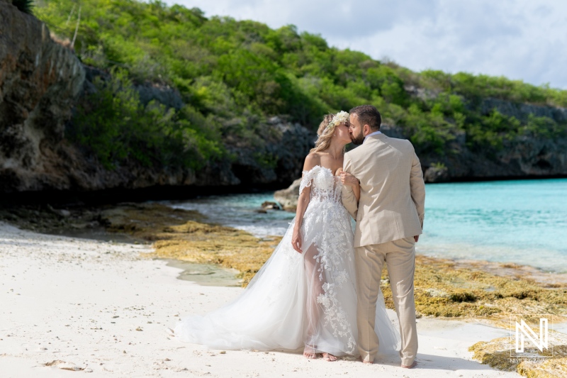 Couple Shares a Romantic Kiss on a Tropical Beach During Their Wedding Celebration Surrounded by Lush Greenery and Clear Blue Waters