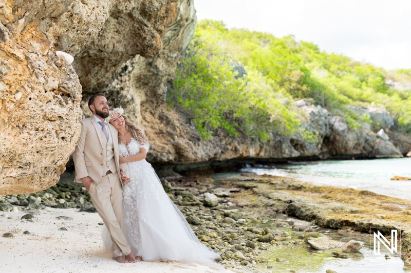 A Couple Celebrating Their Wedding Day on a Scenic Beach With Rocky Cliffs and Lush Green Foliage in the Background During a Sunny Afternoon