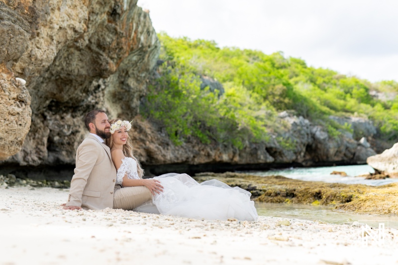 A Couple Joyfully Shares an Intimate Moment on a Serene Beach, Surrounded by Rugged Cliffs and Lush Greenery During a Beautiful Day