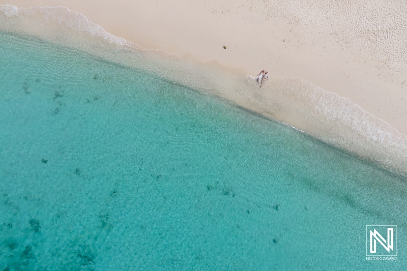 Couple Walking Hand-In-Hand Along a Pristine Sandy Beach Under Clear Skies, With Gentle Waves and Turquoise Waters in a Tropical Paradise During Sunset