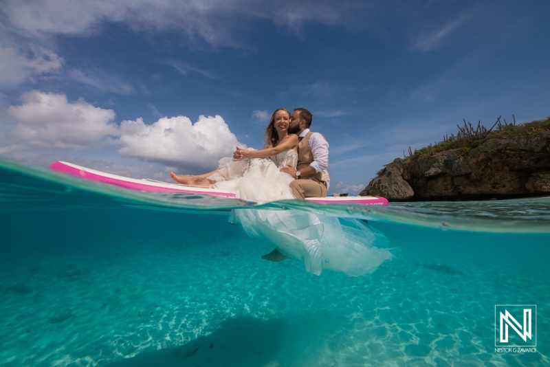 Couple Enjoying a Romantic Paddleboarding Experience in Clear Turquoise Waters While Dressed in Wedding Attire During a Sunny Day at a Tropical Beach