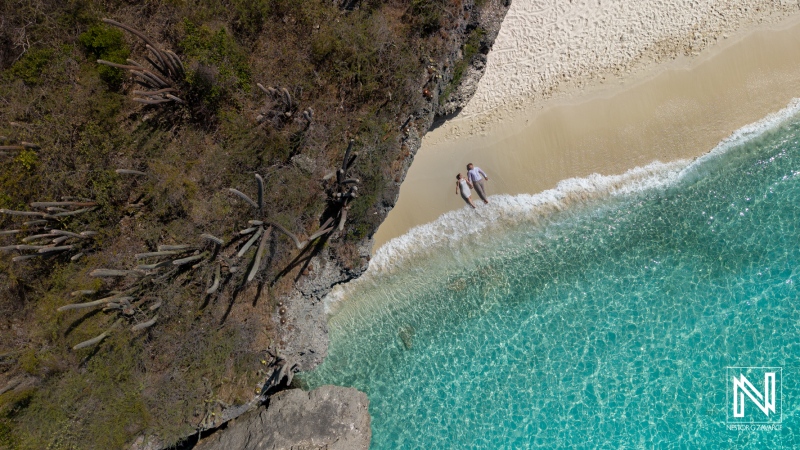 Couple walks on beach during trash the dress session at Cas Abao Beach in Curacao near water and rocks in the background