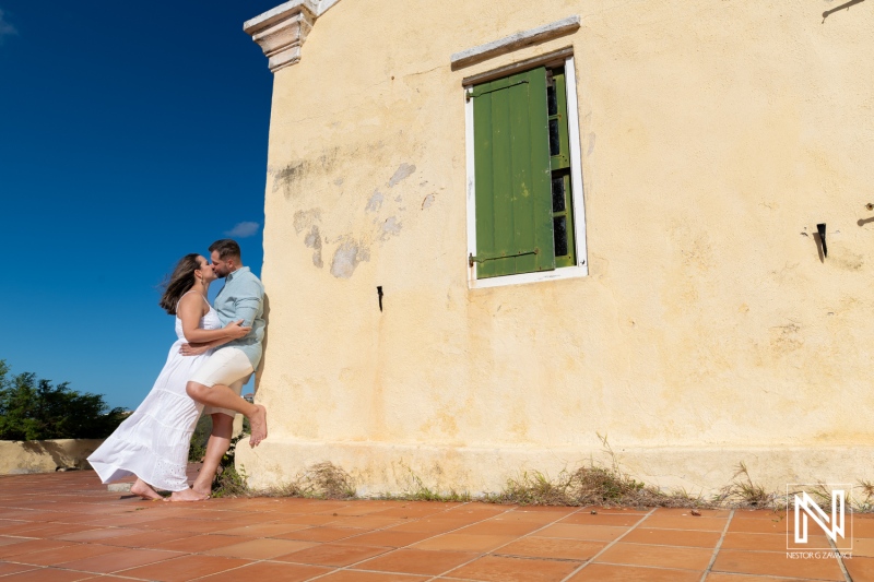 Couple enjoys romantic moment in Cas Abao, Curacao during Trash The Dress experience capturing joy and elegance by rustic building