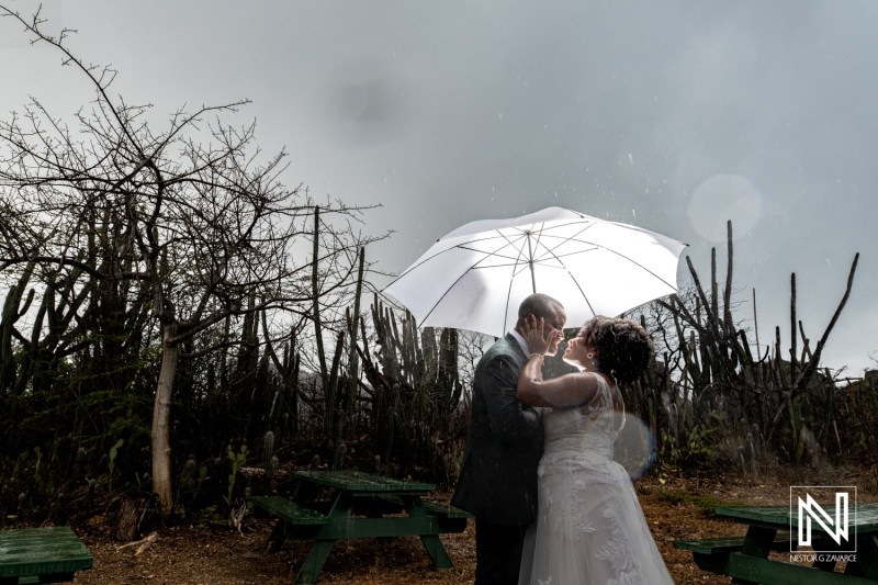 A Couple Embraces Under a White Umbrella During a Rain Shower in a Rustic Outdoor Setting Surrounded by Trees