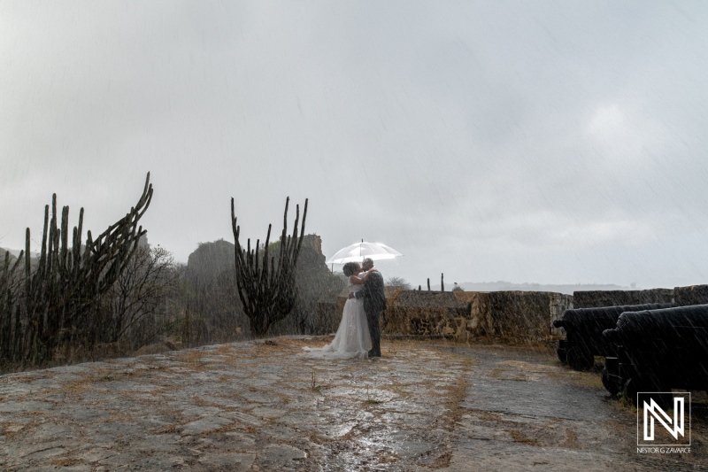 Couple Embraces Under an Umbrella During a Romantic Wedding Ceremony at a Stone Fortress on a Rainy Day