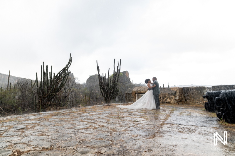 A Couple Embraces Deeply Under the Rain in a Scenic Outdoor Location Surrounded by Cacti, Capturing a Romantic Moment During Their Wedding Day