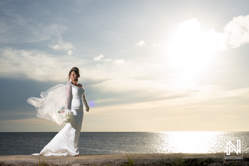 Wearing a beautiful wedding dress, a woman stands by Boka Sami in Curacao, embracing the magic of the Trash the Dress experience against a stunning sunset backdrop