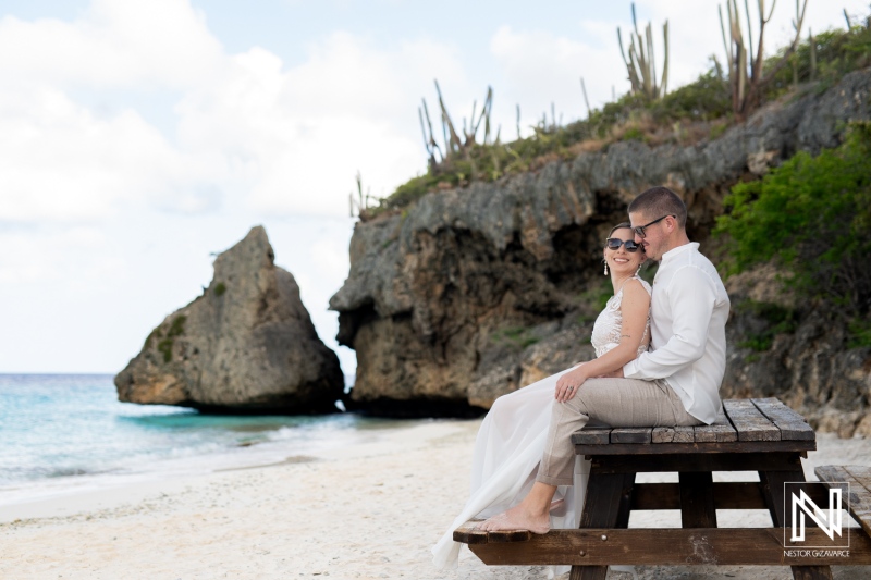 A Couple Enjoys a Romantic Moment on a Secluded Beach While Sitting on a Wooden Bench, Surrounded by Stunning Rock Formations and a Clear Blue Ocean on a Sunny Day