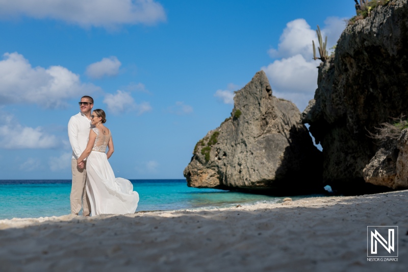 A Couple Stands Hand in Hand on a Picturesque Beach at Sunset, Surrounded by Rocks and Clear Turquoise Waters