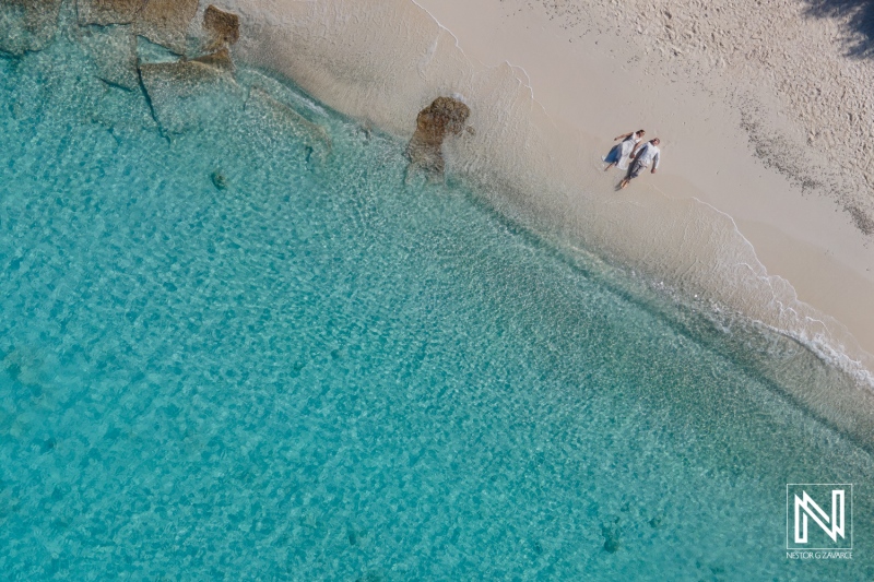 Aerial View of Three Friends Walking Along a Pristine Beach With Clear Turquoise Water on a Sunny Day Near a Tropical Island in the Summer