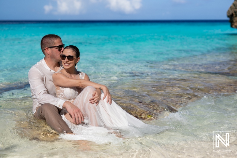 A Romantic Couple Enjoys a Serene Moment Together on a Tropical Beach While Sitting on a Rocky Shoreline Under the Clear Blue Sky