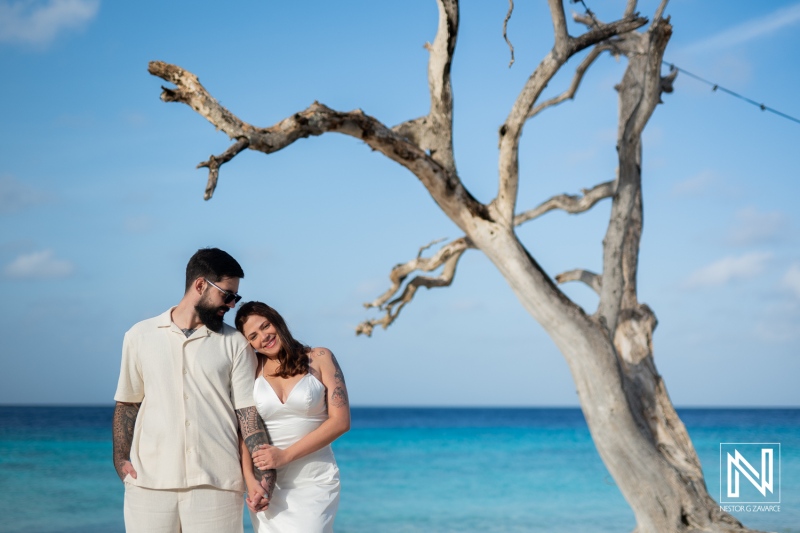 Couple embraces on Cas Abao Beach in Curacao during a Trash the Dress session with vibrant blue waters and unique driftwood backdrop