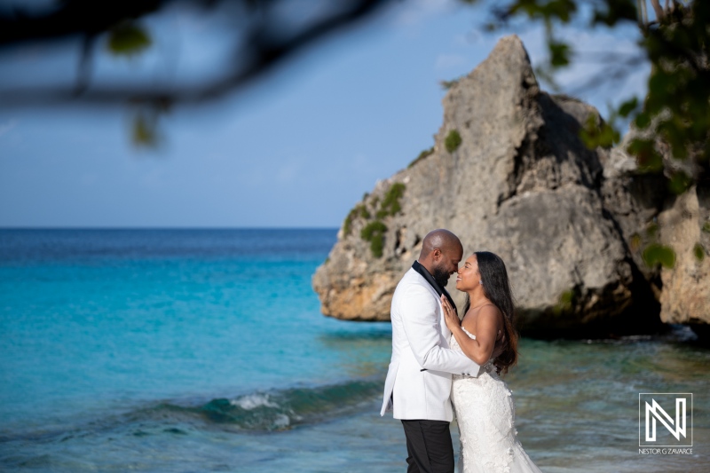 Couple enjoys a trash the dress photoshoot at a beach in Curacao with clear blue water and rocks in the background