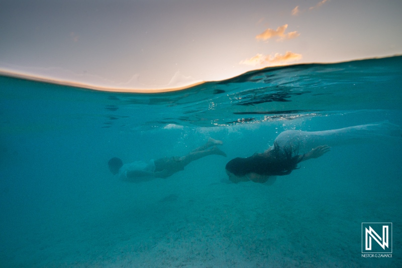 Couple swims underwater during trash the dress photoshoot at Cas Abao Beach in Curacao during sunset