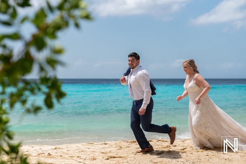 Couple joyfully running along the beach in Curacao during their Trash the Dress session, embracing love and adventure on a sunny day