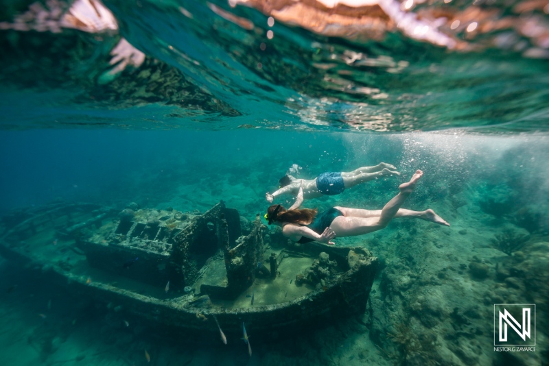 Two people swim over a sunken ship in the waters of Curacao during a clear day