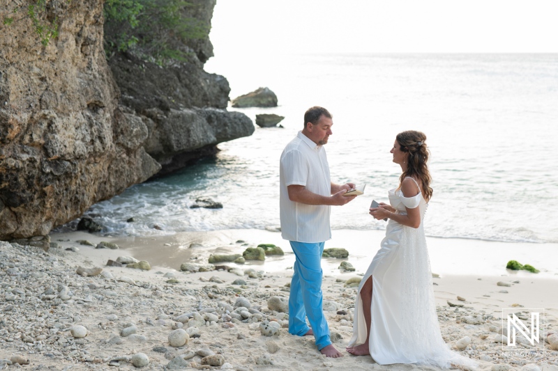 Couple celebrates vow renewal on the pristine beach of Curacao under the soft glow of sunset with natural rocky backdrop