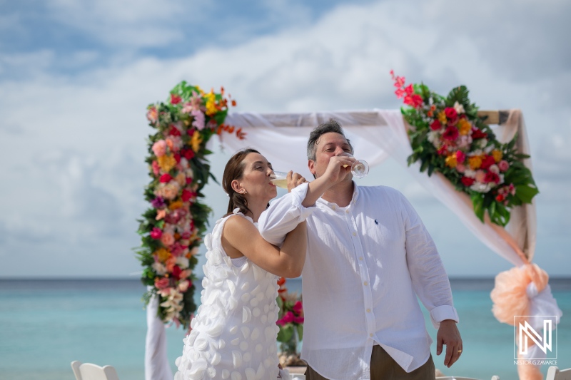 Couple celebrating vow renewal at Cas Abao Beach in Curacao with tropical flowers and champagne