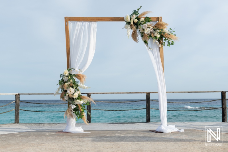 A Beautifully Adorned Wedding Arch With Floral Arrangements Set Against a Serene Ocean Backdrop on a Sunny Day by the Beach, Perfect for a Romantic Ceremony