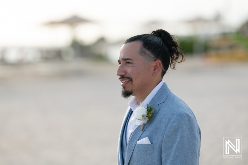 Groom Waiting Anxiously With a Smile on a Beach During a Wedding Ceremony at Sunset, Dressed in a Light Grey Suit With a Boutonniere and a Stylish Hairstyle