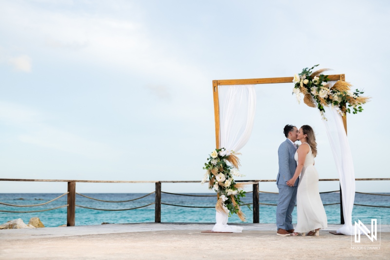 A Couple Exchanges Vows on a Beautiful Seaside Platform Adorned With Floral Decorations During a Serene Sunset Ceremony