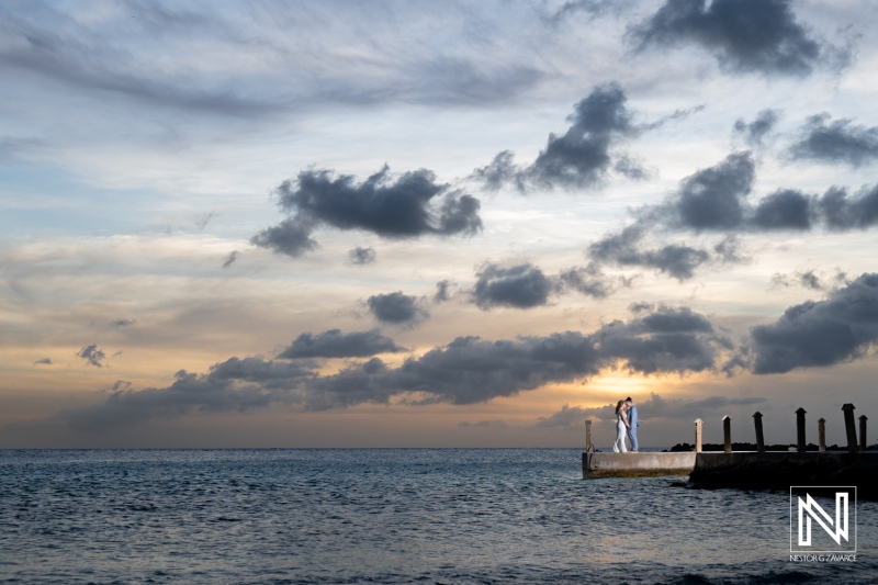 Couple Embracing on a Pier During Sunset With Dramatic Clouds and Calm Ocean Waves, Creating a Romantic Atmosphere in a Coastal Location