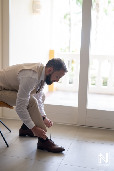 Groom Preparing for Wedding Day by Tying Shoelaces While Seated by Large Windows in a Bright, Airy Venue Reflecting Early Morning Light