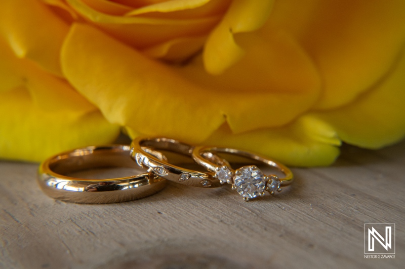 Beautiful Wedding and Engagement Rings Resting Beside a Vibrant Yellow Rose on a Wooden Surface, Showcasing Intricate Designs and a Sparkling Diamond Centerpiece